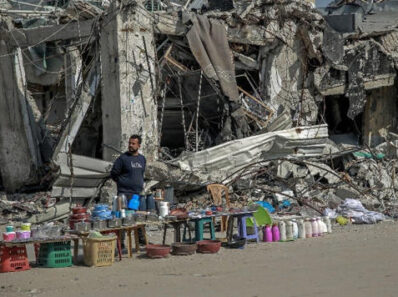 Bidons d'eau vides devant un bâtiment en ruines à Gaza